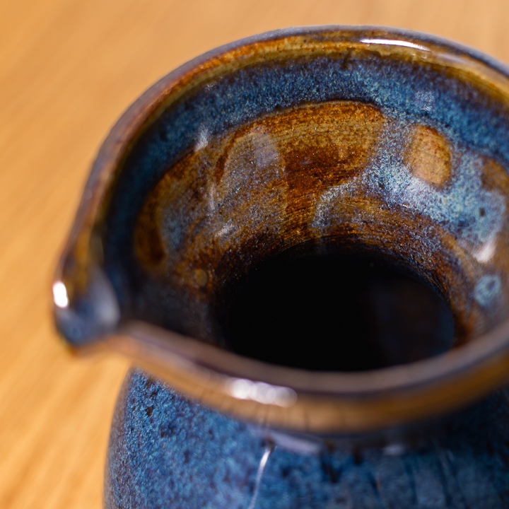 Close-up of a ceramic pitcher with a textured surface on a wooden table.