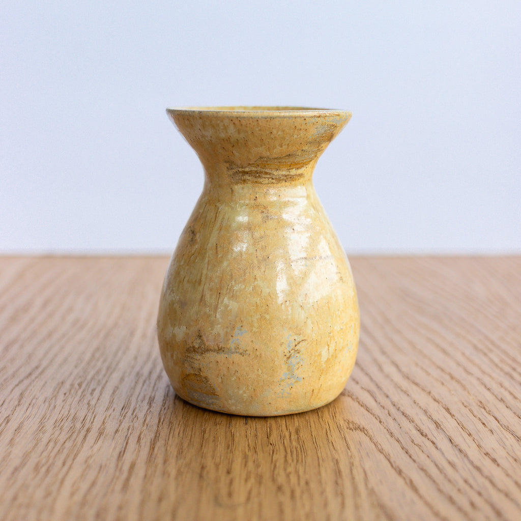 Yellow ceramic vase on a wooden surface with a light blue background