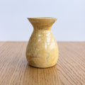 Yellow ceramic vase on a wooden surface with a light blue background