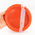 Hand holding an orange ceramic plate with white details against a white background