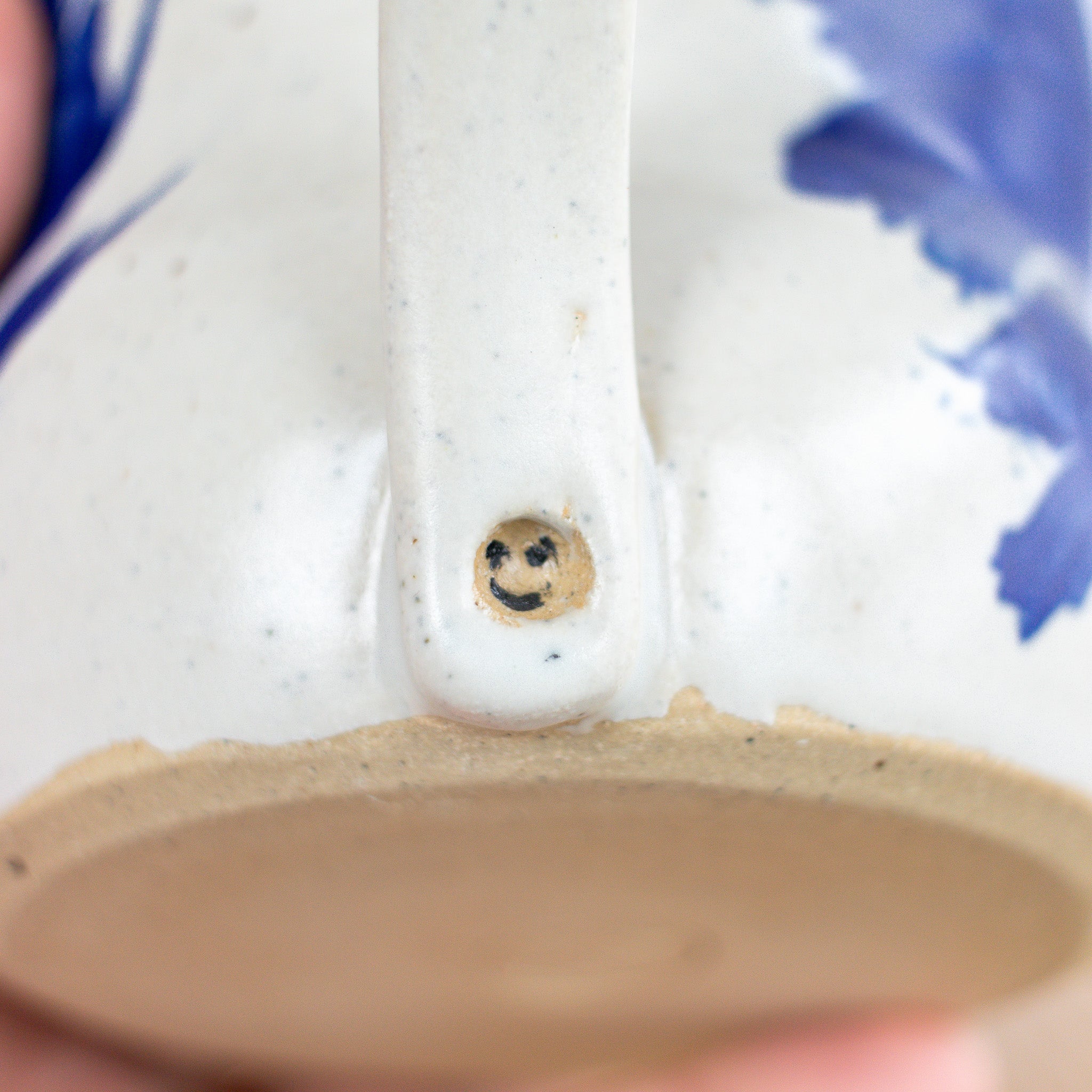 Close-up of a ceramic teapot with a smiley face design on the spout.