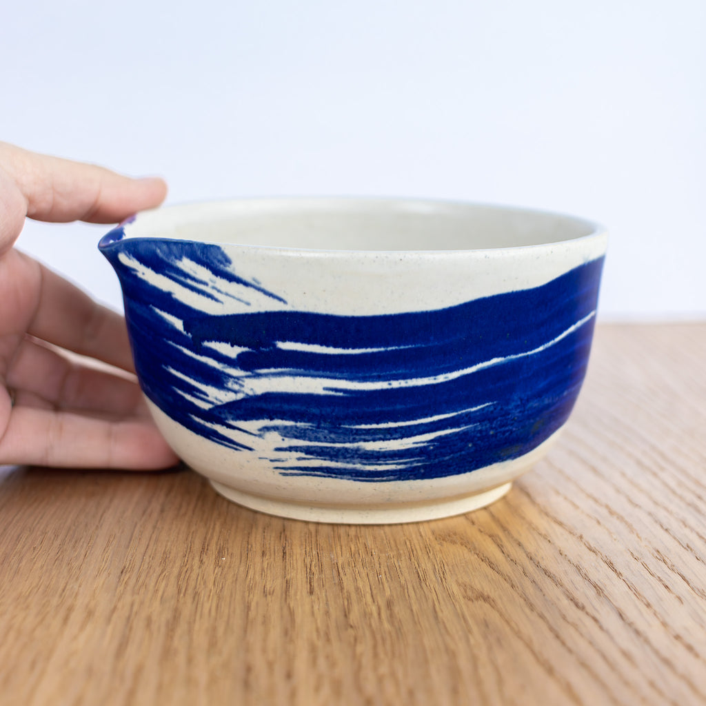 Ceramic bowl with blue and white design held by a hand on a wooden surface.