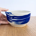 Ceramic bowl with blue and white design held by a hand on a wooden surface.
