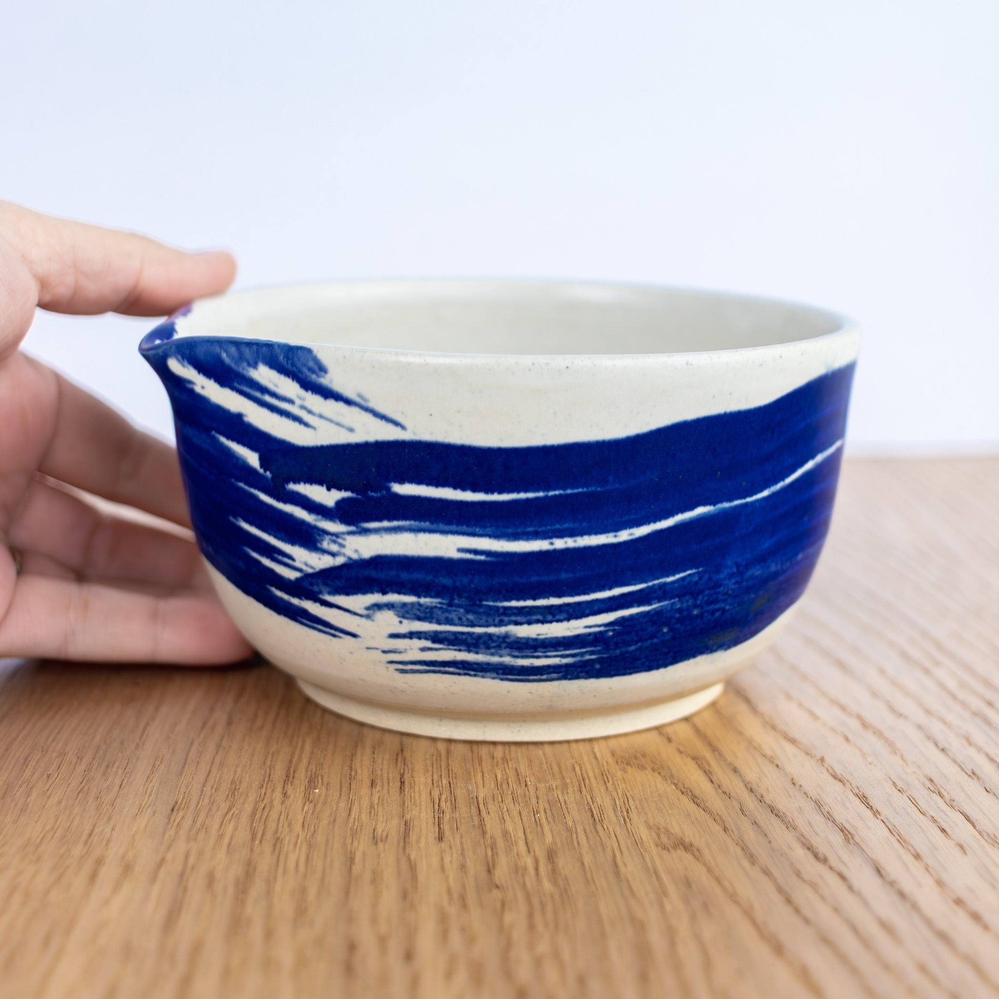 Ceramic bowl with blue and white design held by a hand on a wooden surface.